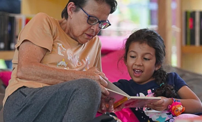 Mujer y niña leen juntas un libro en una biblioteca de Comfama